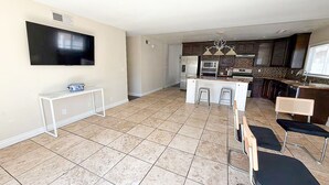A spacious living area with a flat-screen TV, a small white console table, and a kitchen with dark cabinets, a microwave, and a refrigerator. - Simi Valley Pool Home Spacious & Fully Furnished 4bd 2ba (Simi Valley)