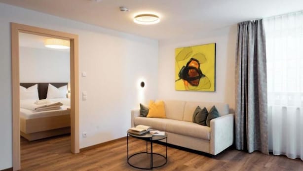 A modern hotel room with a wooden floor, a sofa with cushions, a small round table, and a painting on the wall. - Versail D1 Apartment (Gaschurn)