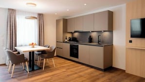 A modern kitchen with a dining table and chairs, built-in appliances, and a flat-screen TV mounted on the wall. - Versail D1 Apartment (Gaschurn)