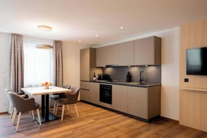 Eine moderne Küche mit Esstisch und Stühlen, integrierten Geräten und einem an der Wand befestigten Flachbildfernseher.