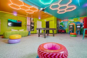 Ein helles Zimmer mit einem grünen Sofa, einem Tisch und einer farbenfrohen Wand mit sechseckigen Lampen.