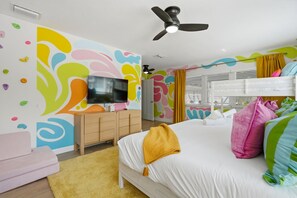 Ein Schlafzimmer mit einem Bett, einem Fernseher, einem Kleiderschrank, einem Deckenventilator und farbenfroher Wandgestaltung.