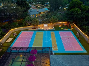 Un terrain multisports doté de terrains de basketball et de tennis, entouré d’une clôture et illuminé par des guirlandes lumineuses.