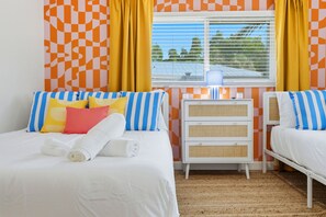 Une chambre d’hôtel avec deux lits, une commode blanche et une fenêtre avec des rideaux jaunes.