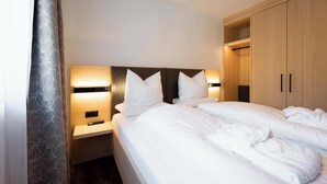 Hotellihuone, jossa on sänky, yöpöydät, vaatekaappi ja lehvikuvioitu verho.