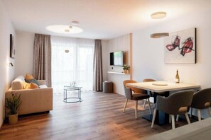 Ein modernes Wohnzimmer mit einer Couch, einem Esstisch, Stühlen und einem Fernseher an der Wand.