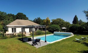 Uma casa com piscina, alpendre coberto e gramado.