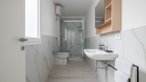 Ein schmales Badezimmer mit Toilette, Dusche und Waschbecken.