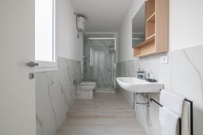 Ein schmales Badezimmer mit Toilette, Dusche und Waschbecken.