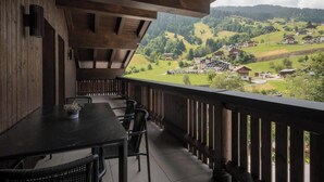 A wooden balcony with a table and chairs, overlooking a village with houses and greenery. - Apartment Zamangspitze 32 (Gaschurn)