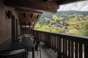 A wooden balcony with a table and chairs, overlooking a village with houses and greenery. - Apartment Zamangspitze 32 (Gaschurn)