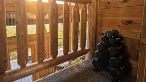 A wooden cabin interior with a staircase leading to a deck, a stack of dumbbells, and a view of the outdoors. - Smoky Mtn Views  Hot Tub  Sauna Game Room (Sevierville)
