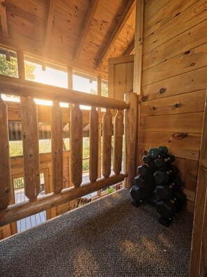 Ein Holzblockhaus-Interieur mit einer Treppe zu einer Terrasse, einer Sammlung von Kurzhanteln und Blick ins Freie.