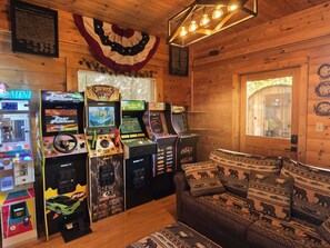 Ein Zimmer mit Holzwänden, einer Couch mit Tiermotiven und Spielautomaten, darunter 'The Fast and the Furious' und 'Big Buck Hunter'.