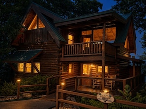 A two-story log cabin with a balcony, a sign indicating 'Brother's Cove Breathtaking 36', and a well-lit entrance. - Smoky Mtn Views  Hot Tub  Sauna Game Room (Sevierville)