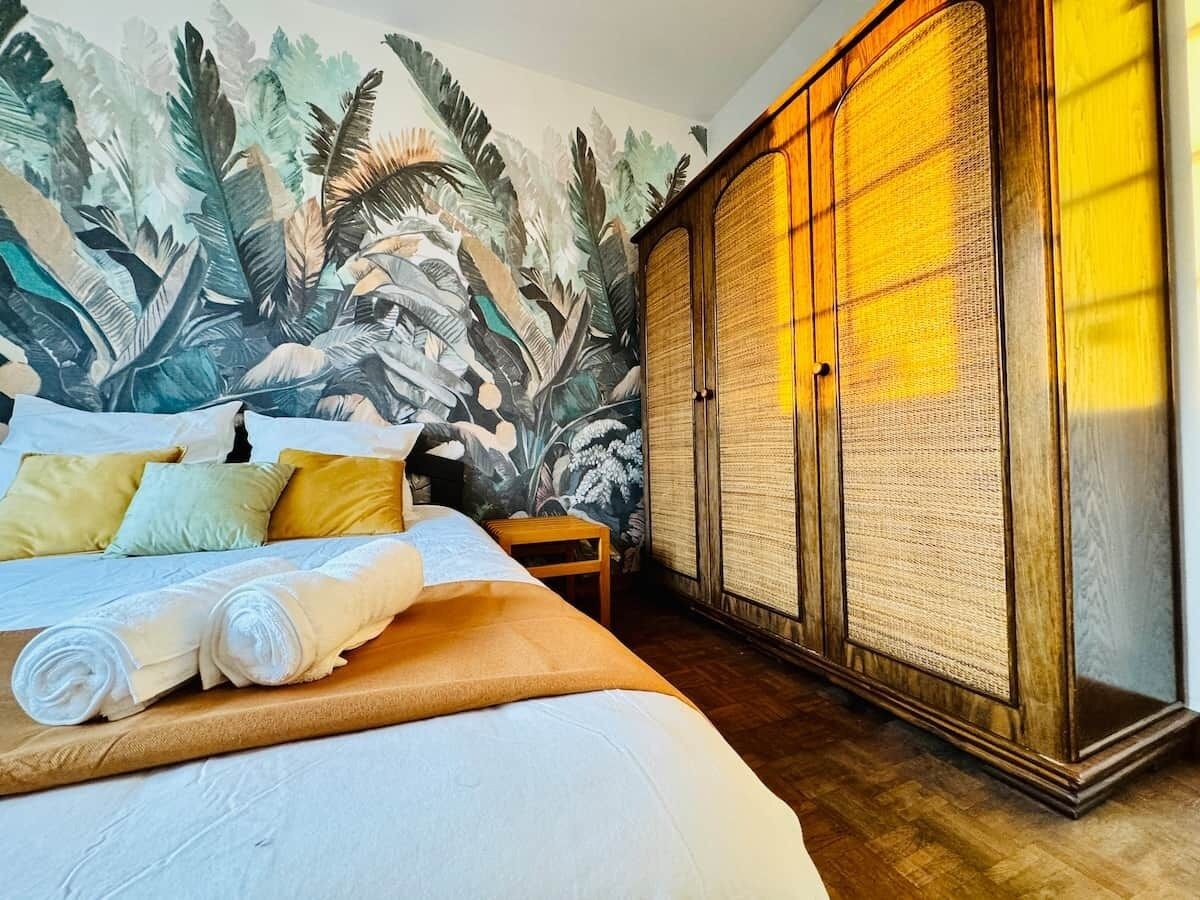 A hotel room with a bed, a wall mural, a wardrobe, and a wooden floor.