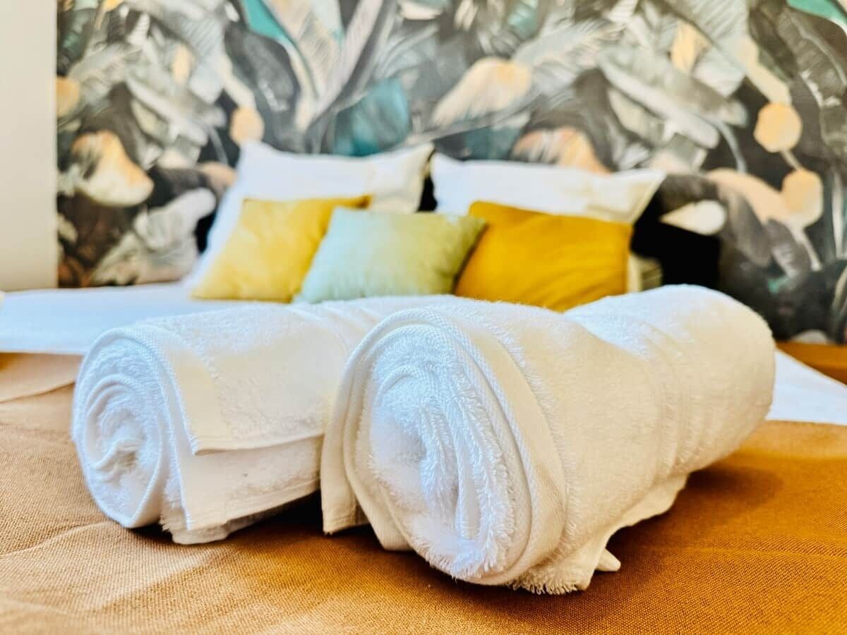 Ein Bett mit aufgerollten weißen Handtüchern und einer Wand mit Muster im Hintergrund.