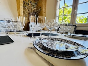A dining table set with multiple wine glasses and plates, a vase with dried plants, and a window with a view of trees. - Logement 100m² - La Villa' Tyno - 9 couchages (La Teste-de-Buch)