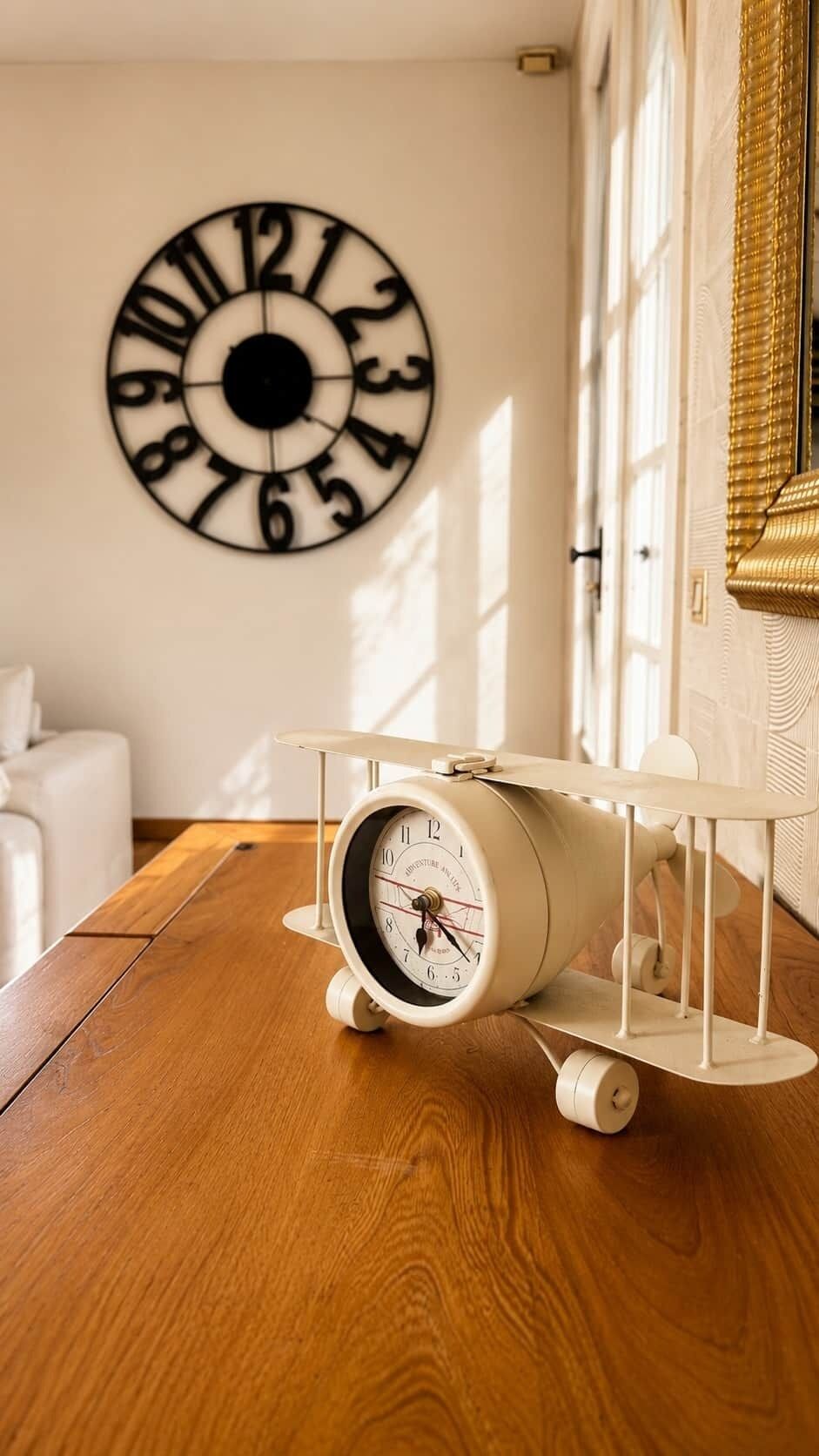 Une pièce avec un plancher en bois, une table blanche, une horloge et une fenêtre avec des rideaux.