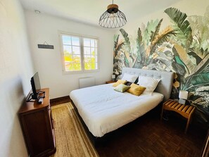 Ein Schlafzimmer mit Bett, Nachttisch, Schreibtisch, einem Fenster und einer Wandmalerei.