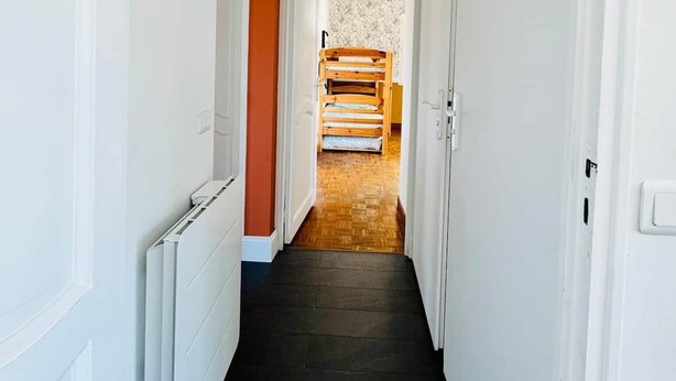 A narrow hallway with a radiator on the left, a wooden bed in the background, and a ceiling fan with a flower design. - Logement 100m² - La Villa' Tyno - 9 couchages (La Teste-de-Buch)
