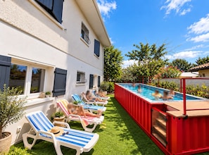 A swimming pool adjacent to a building with multiple lounge chairs and potted plants. - Logement 100m² - La Villa' Tyno - 9 couchages (La Teste-de-Buch)