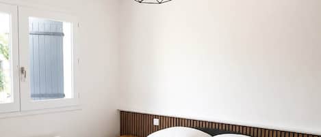Ett sovrum med en stor säng, två sängbord, en hängande lampa och ett fönster med utsikt.