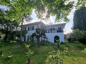 A two-story building with a balcony, surrounded by greenery and trees. - Logement RDC - La Villa Tyno Evasion - 60m² (La Teste-de-Buch)