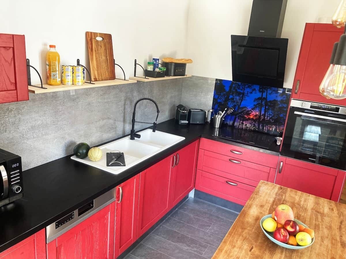 A kitchen with red cabinets, a black countertop, a sink, and a wooden table with fruit.