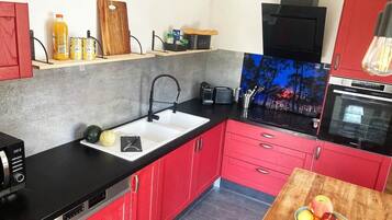 A kitchen with red cabinets, a black countertop, a sink, and a wooden table with fruit.