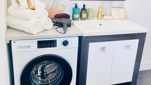 Pieni, käytännöllinen hotellin kylpyhuone, jossa on pesukone, pesuallas ja peili.