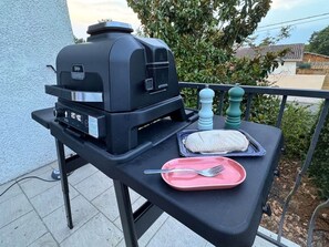 A barbecue grill on an outdoor table with a pink plate and utensils, and a salt and pepper shaker. - Villa' Tyno Excellence familiale - 18 couchages (La Teste-de-Buch)