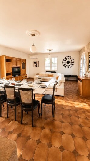 Amplia sala de estar con una mesa de comedor lista para seis personas, un sofá y un gran reloj de pared.