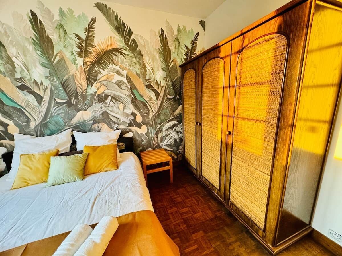 A bedroom with a bed, a nightstand, a wardrobe, and a mural on the wall.