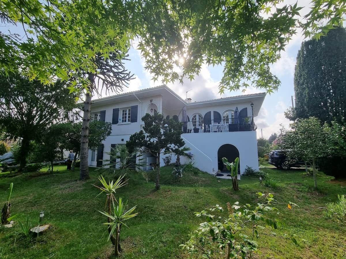 Um edifício de dois andares com varanda, cercado por vegetação e árvores.