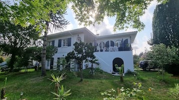 Um edifício de dois andares com varanda, cercado por vegetação e árvores.