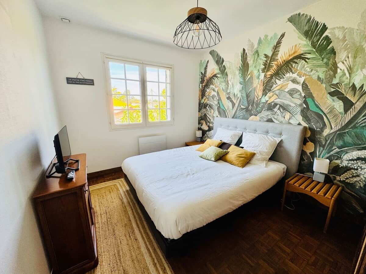 A bedroom with a bed, a nightstand, a desk, a window, and a wall mural.