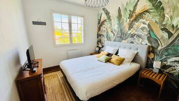 A bedroom with a bed, a nightstand, a desk, a window, and a wall mural.