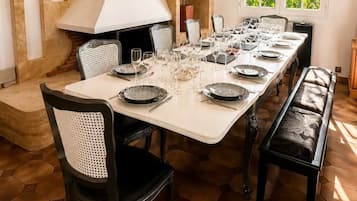Et spiseområde med et langt bord dækket til måltid, stole, en dekorativ loftlampe og et vindue med udsigt til grønne omgivelser.