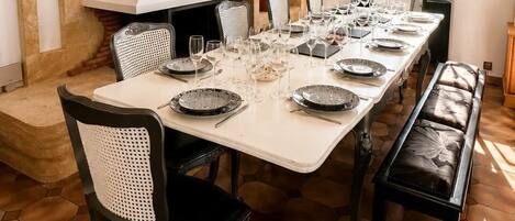 Un comedor con una larga mesa dispuesta para una comida, sillas, una lámpara decorativa en el techo y un ventanal con vista a follaje.