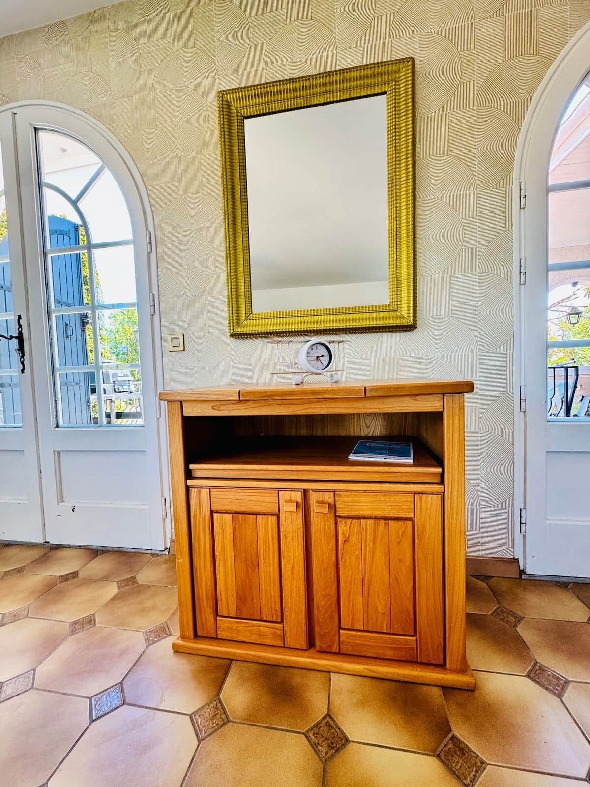 Un meuble en bois contenant une horloge, un miroir et une porte ornée d’un motif géométrique.
