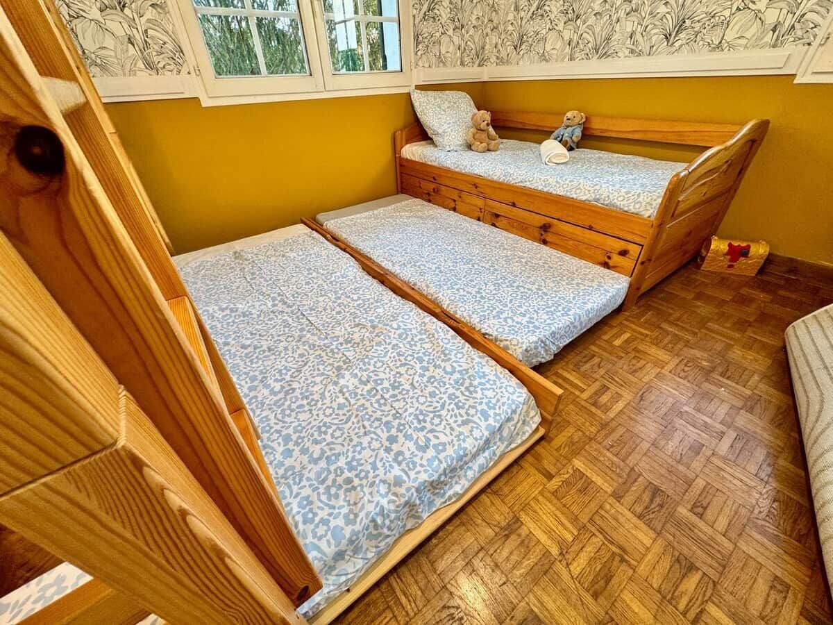 A room with two wooden bunk beds, a window with a view, and a patterned floor.