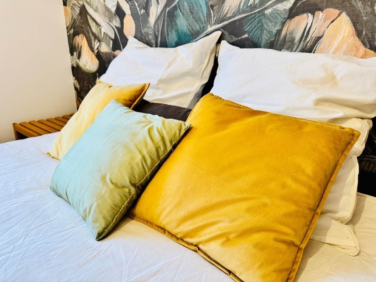 Ein Bett mit zwei Kissen, eines hellgrün und eines gelb, und einem Kopfstück mit einem Blumenmuster.
