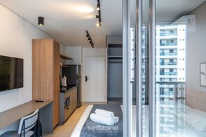 A modern hotel room with a bed, a desk, a kitchenette, and a sliding door to a balcony. - Comfort in Condo. w/ Pool & Balcony Lss1319 (São Paulo)