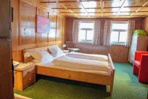 Ein Zimmer mit Holzboden, einem Bett, einem Sessel und einem Fenster.