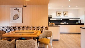 Un comedor con mesa de madera y sillas estampadas, una cocina con electrodomésticos modernos, y una pared con un cuadro de pájaros.