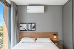 A hotel room with a bed, a wall-mounted air conditioner, two framed artworks, a bedside lamp, and a window with curtains. - Comfort in Condo. w/ Pool and Balcony Lss1318 (São Paulo)