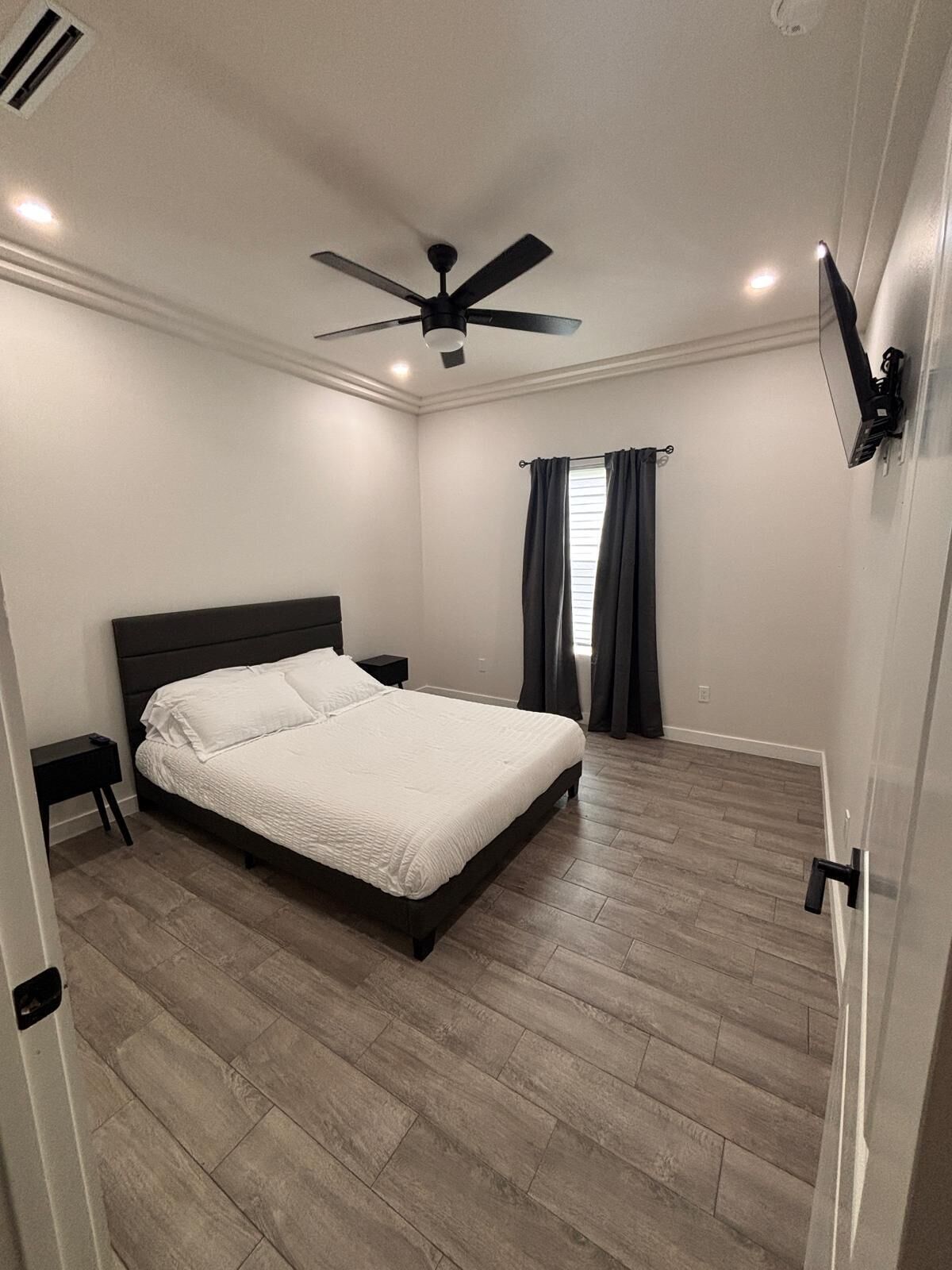 A bedroom with a bed, a nightstand, a ceiling fan, and a window with curtains.
