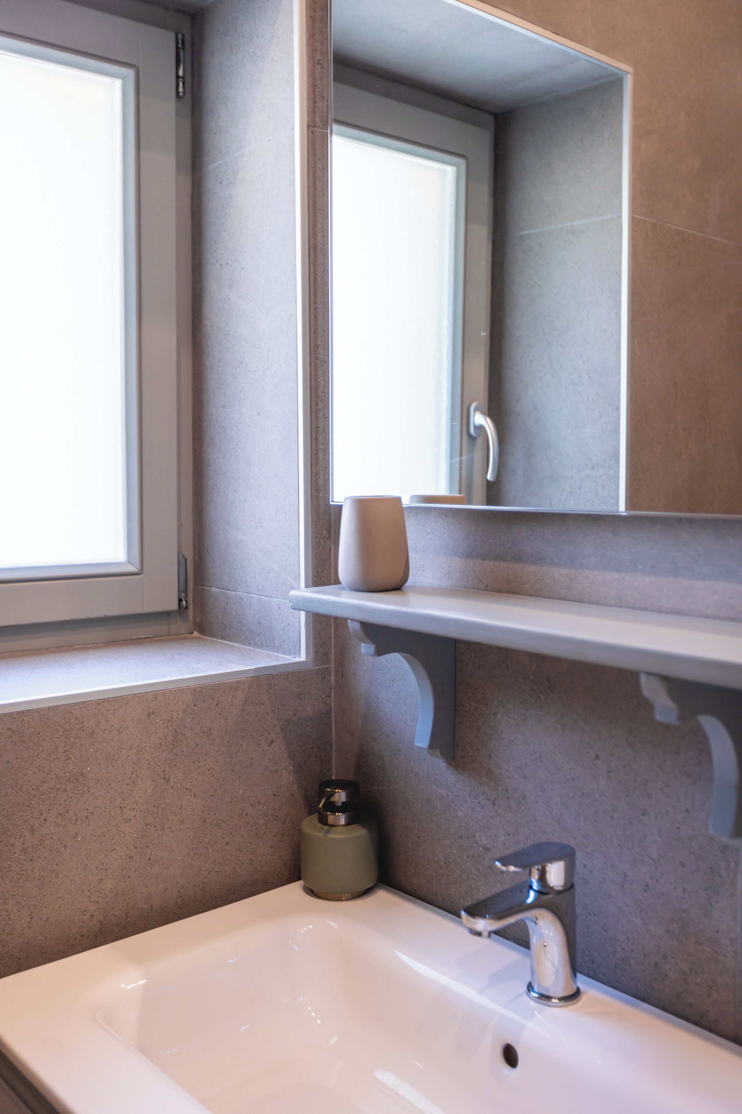 A bathroom with a white sink, a mirror, and a window.