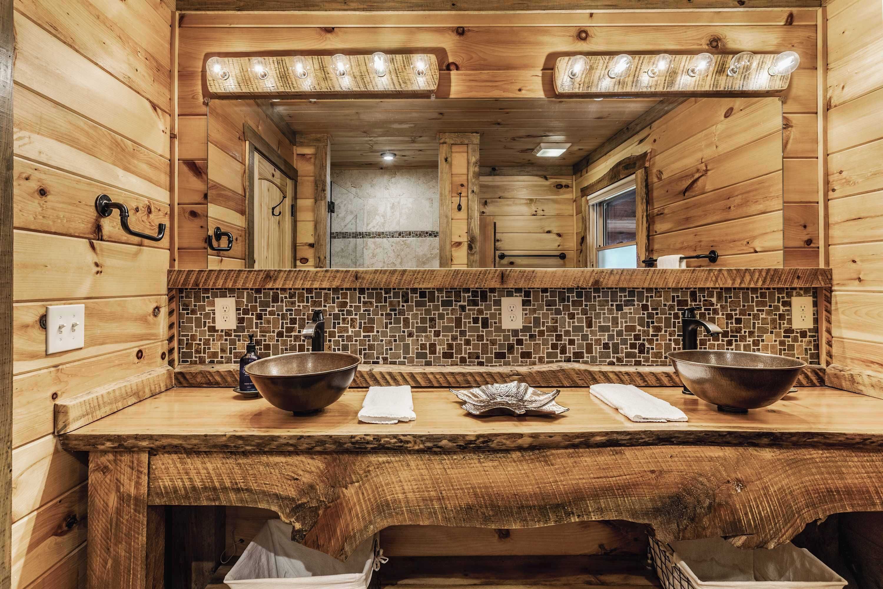 Baño de cabaña de madera con un espejo grande, dos lavamanos y un salpicadero de azulejos.